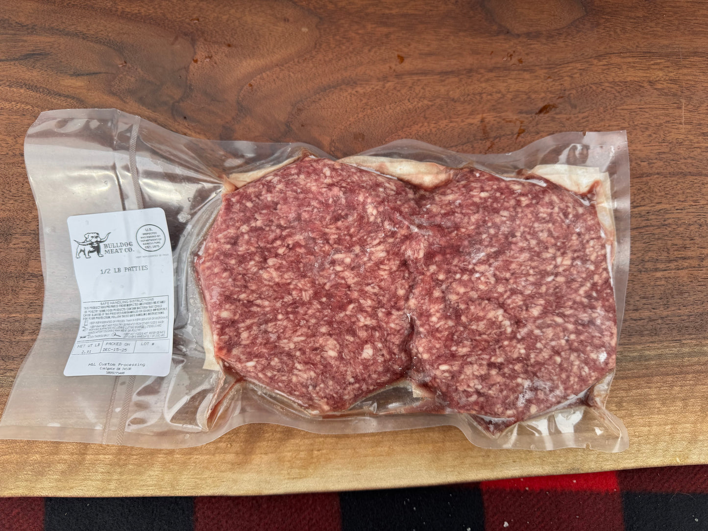 Two raw meat patties in a vacuum-sealed package on a wooden surface