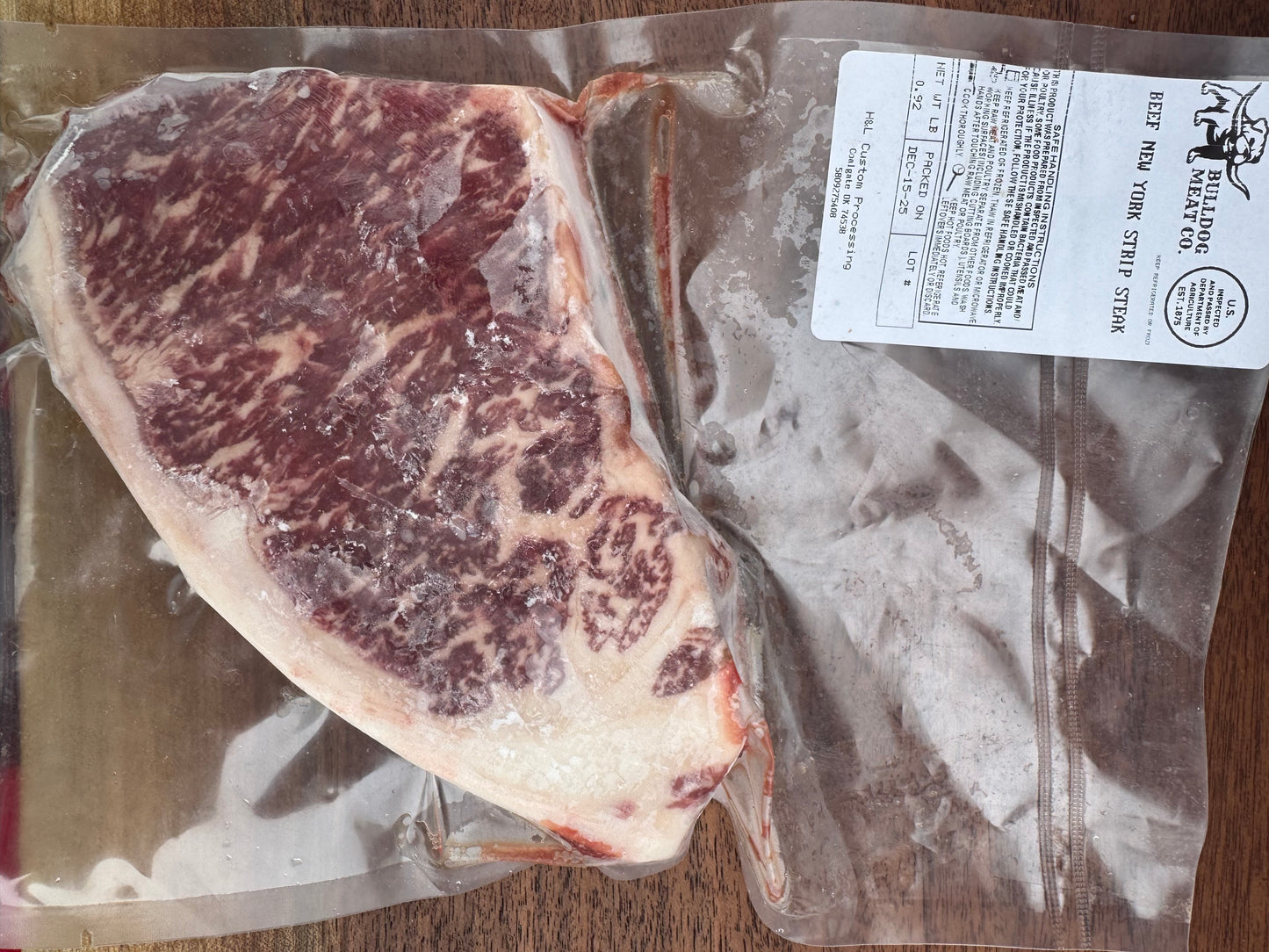 Vacuum-sealed raw NY strip steak with a label on a wooden surface