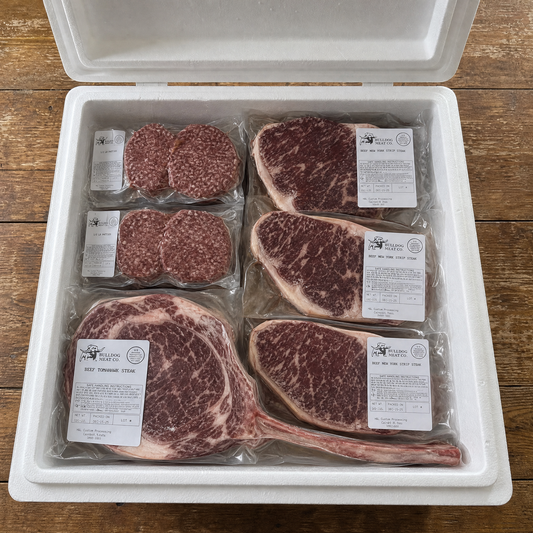 Packaged meat including steaks and burgers in a white container on a wooden surface