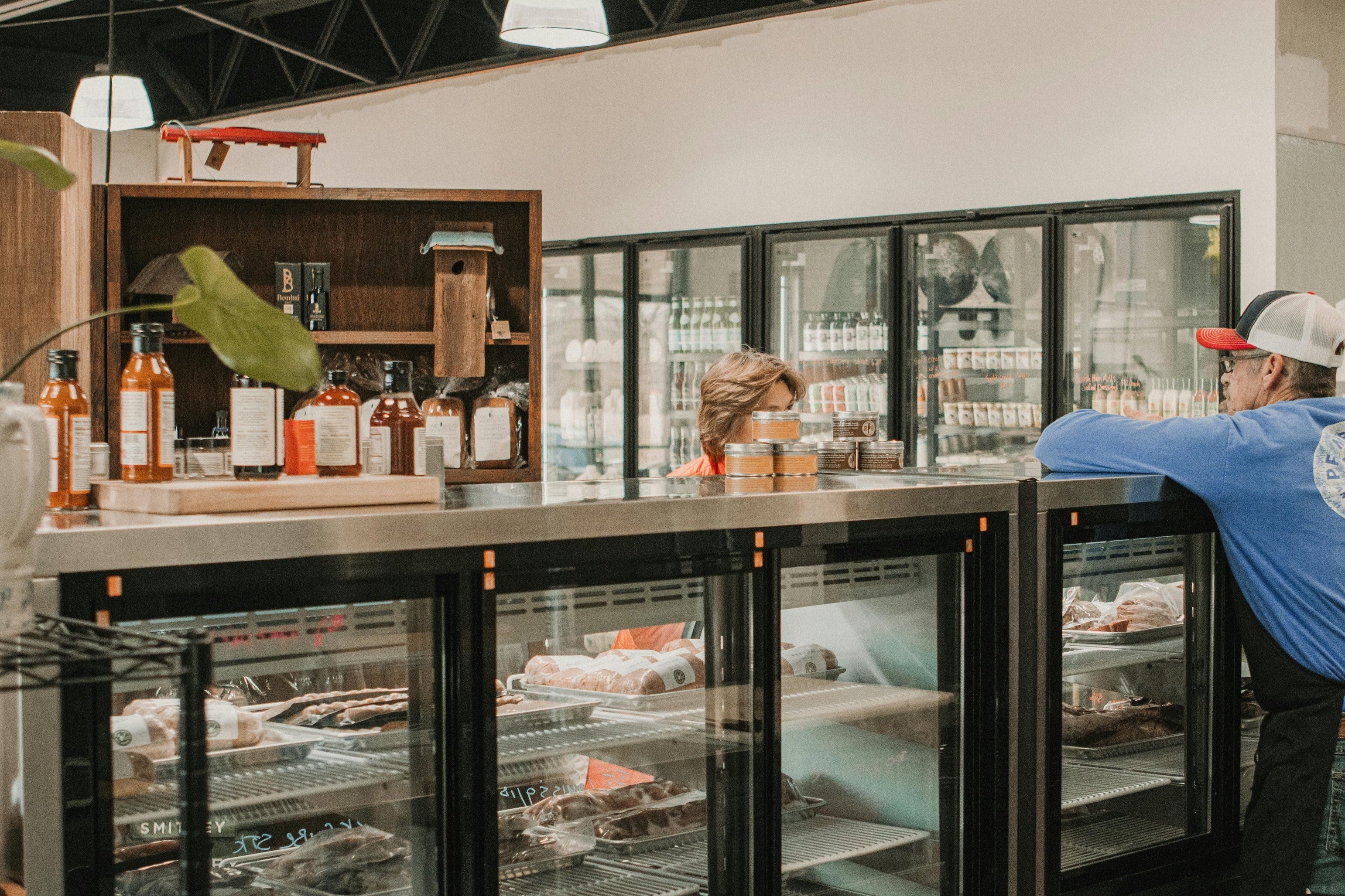 Person in a blue shirt leaning against a counter with shelves displaying various items.